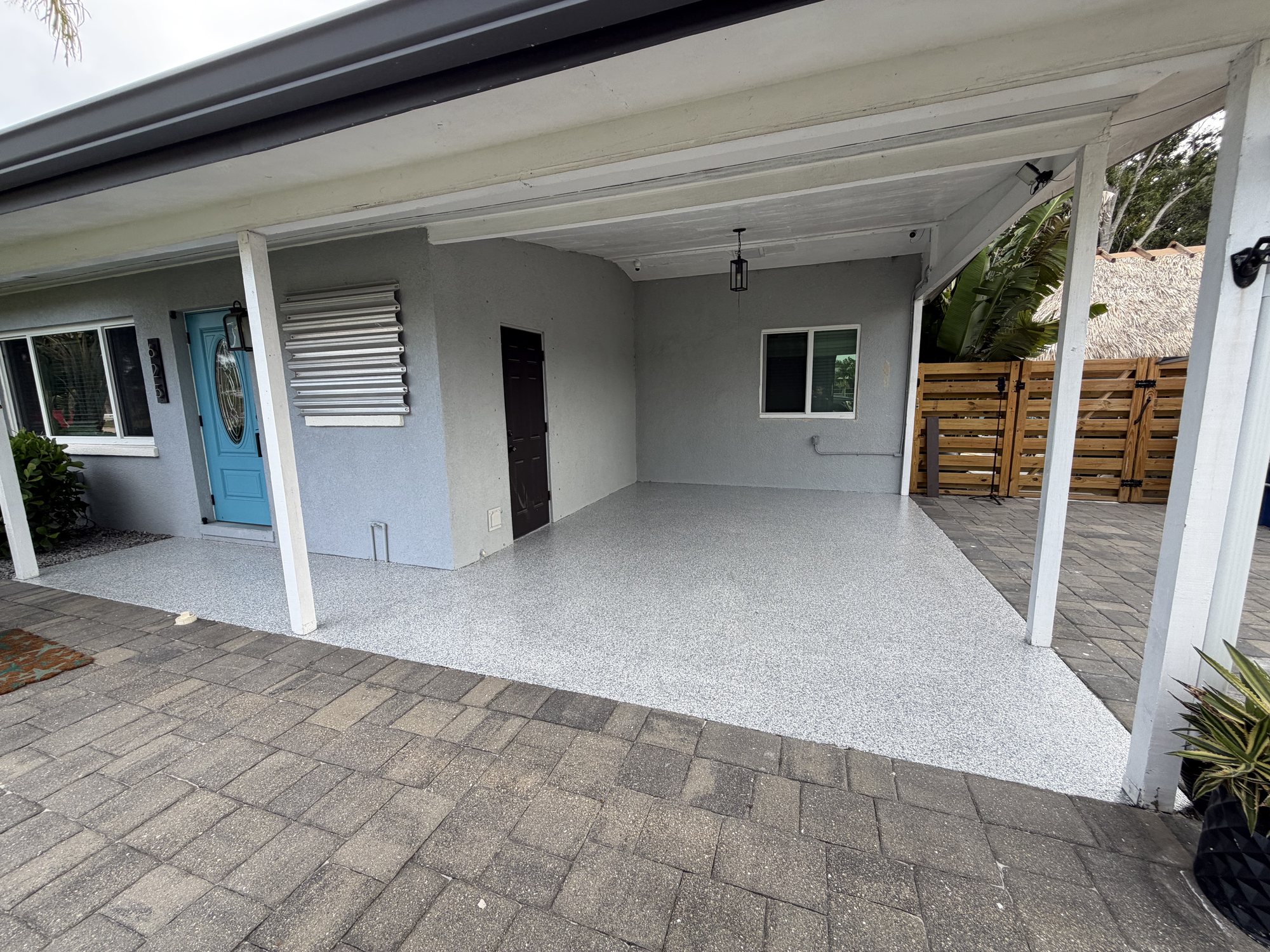Flake coating on a covered carport slab beside a mid-century Florida house with a teal front door