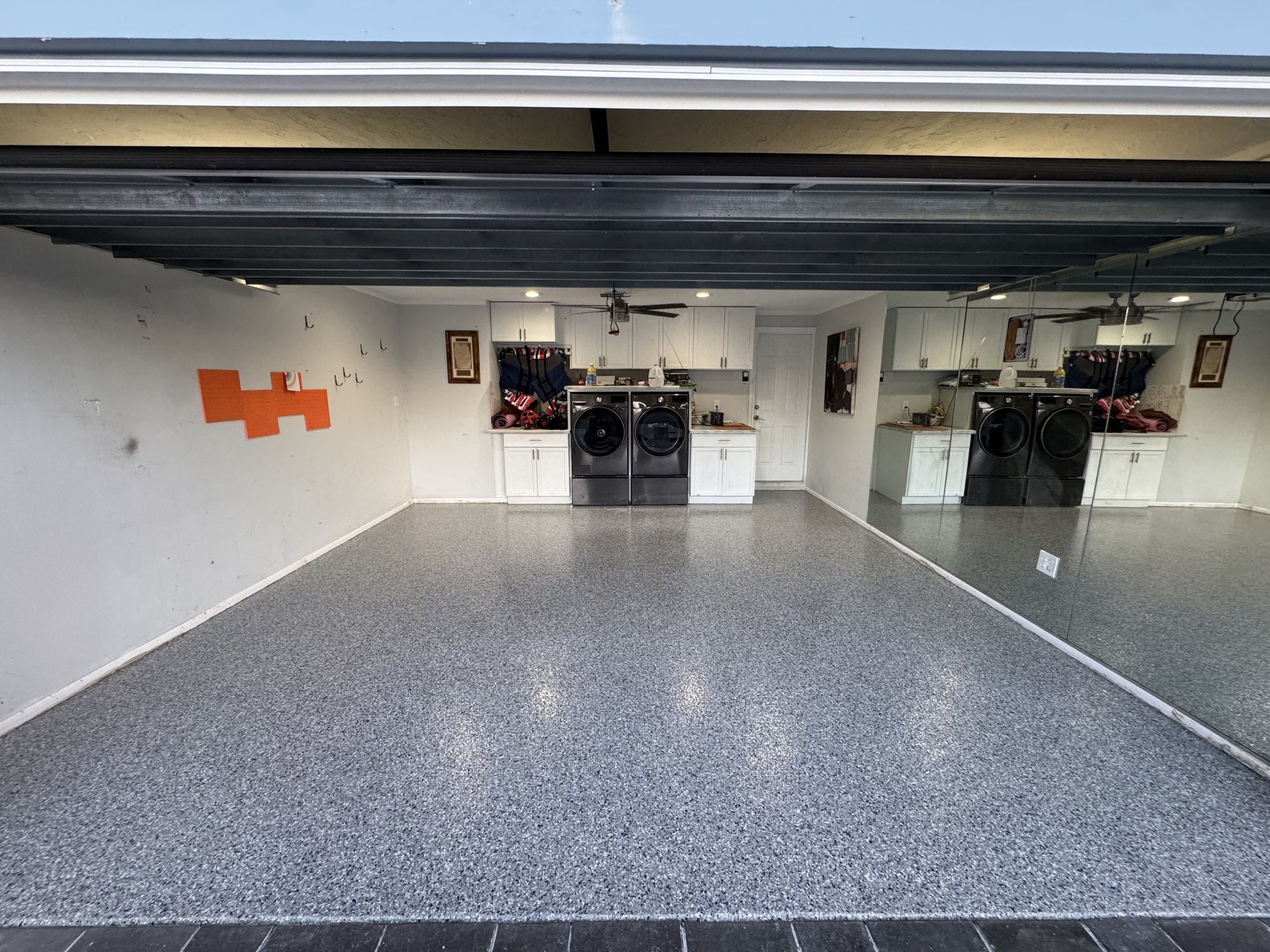 Gray flake floor in a garage finished as a laundry and utility room, cabinetry, washer and dryer and a mirrored wall