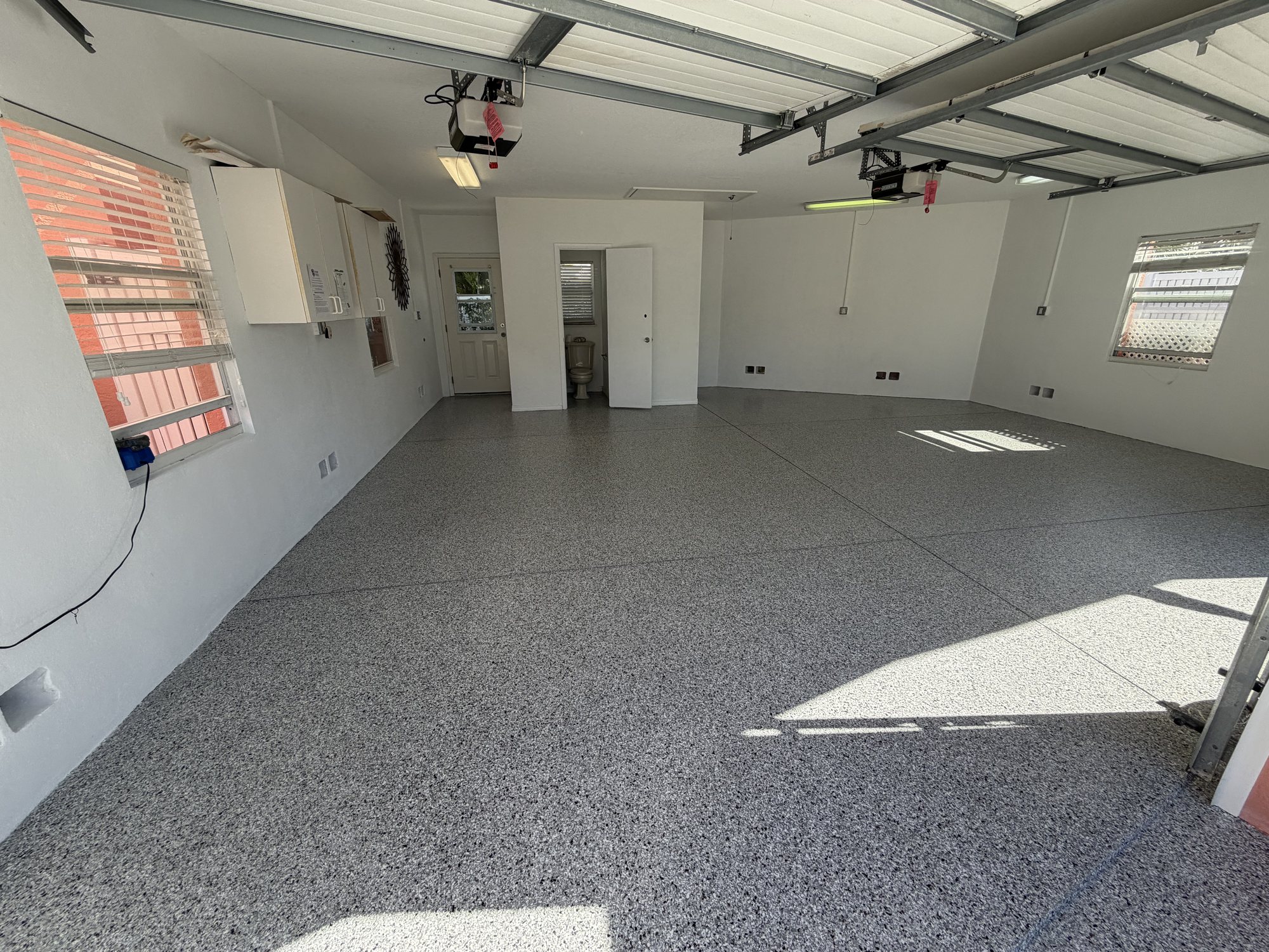 Gray flake floor across a large multi-bay garage workshop with wall cabinets and two opener rails overhead