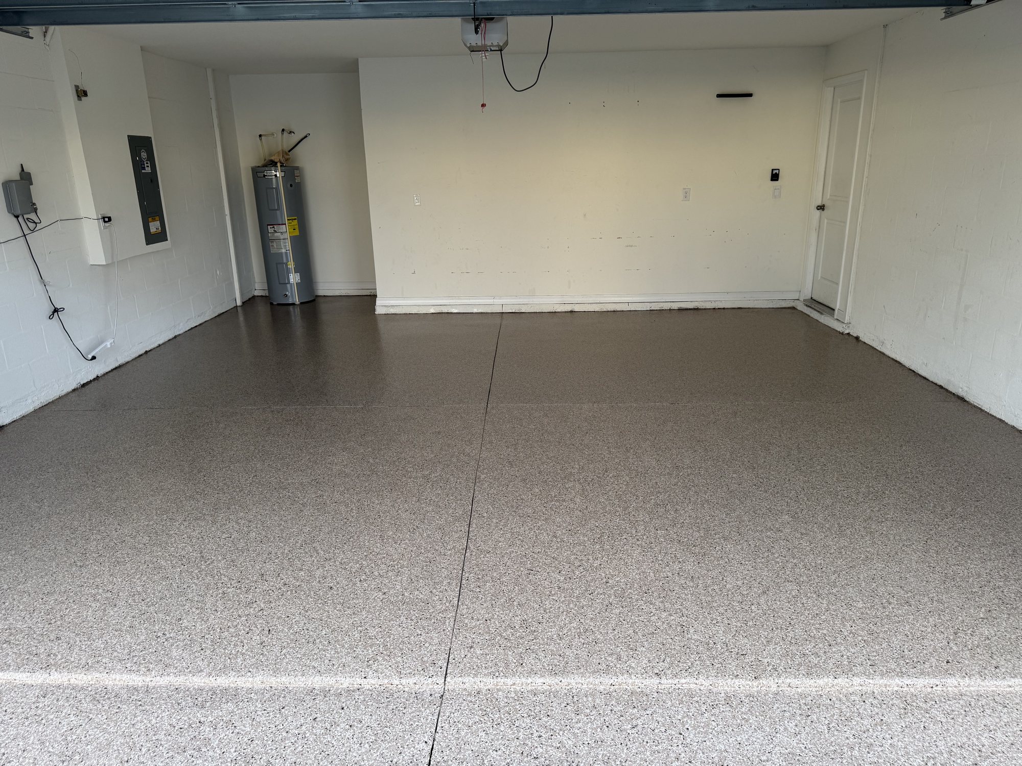 Tan and sand flake garage floor lit warm at night, white block walls and a water heater in the corner