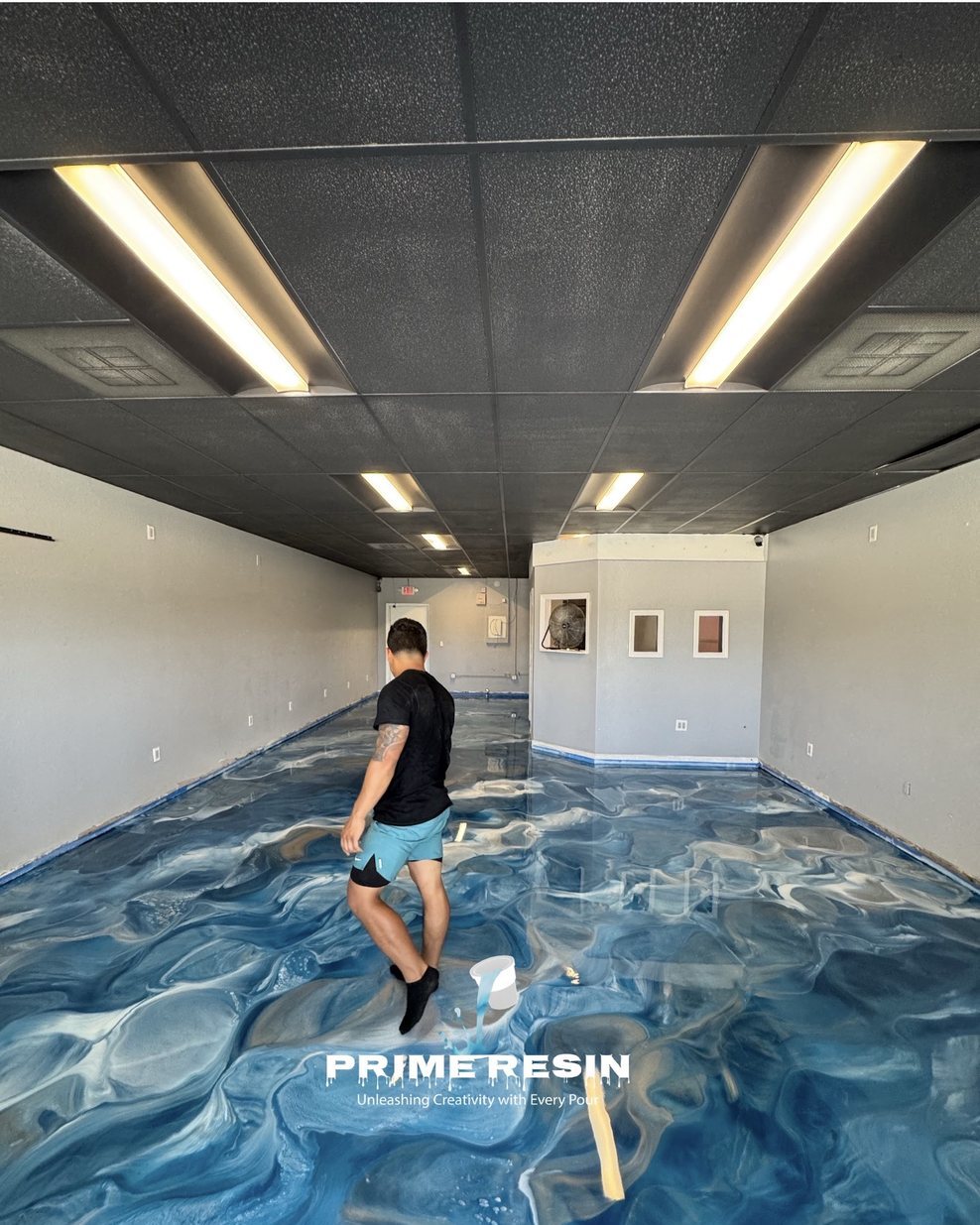Prime Resin installer walking a freshly poured blue and white metallic floor in a commercial unit under drop-ceiling lighting