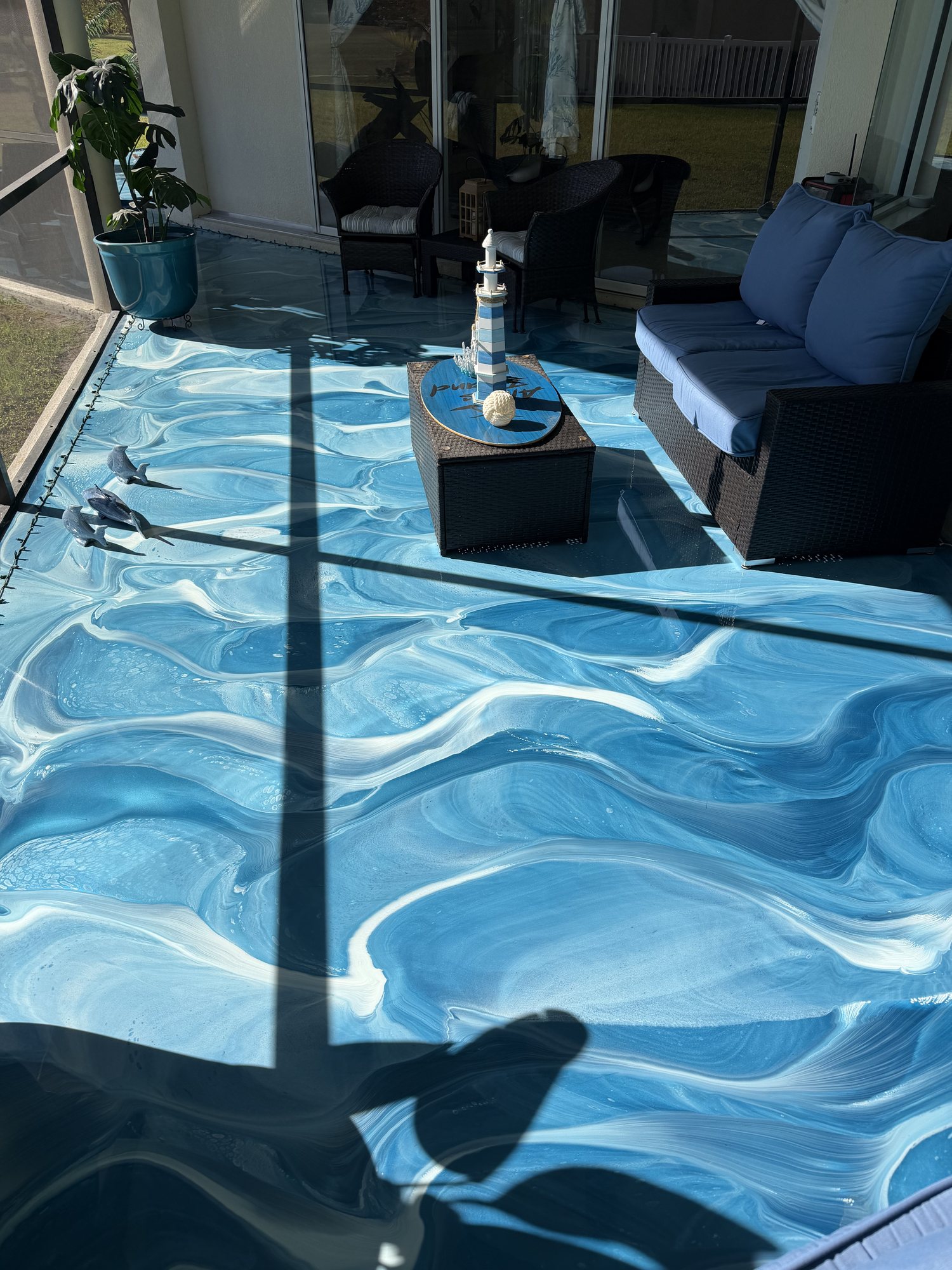 Blue and white wave-poured metallic floor on a furnished screened lanai with wicker seating and a lighthouse ornament