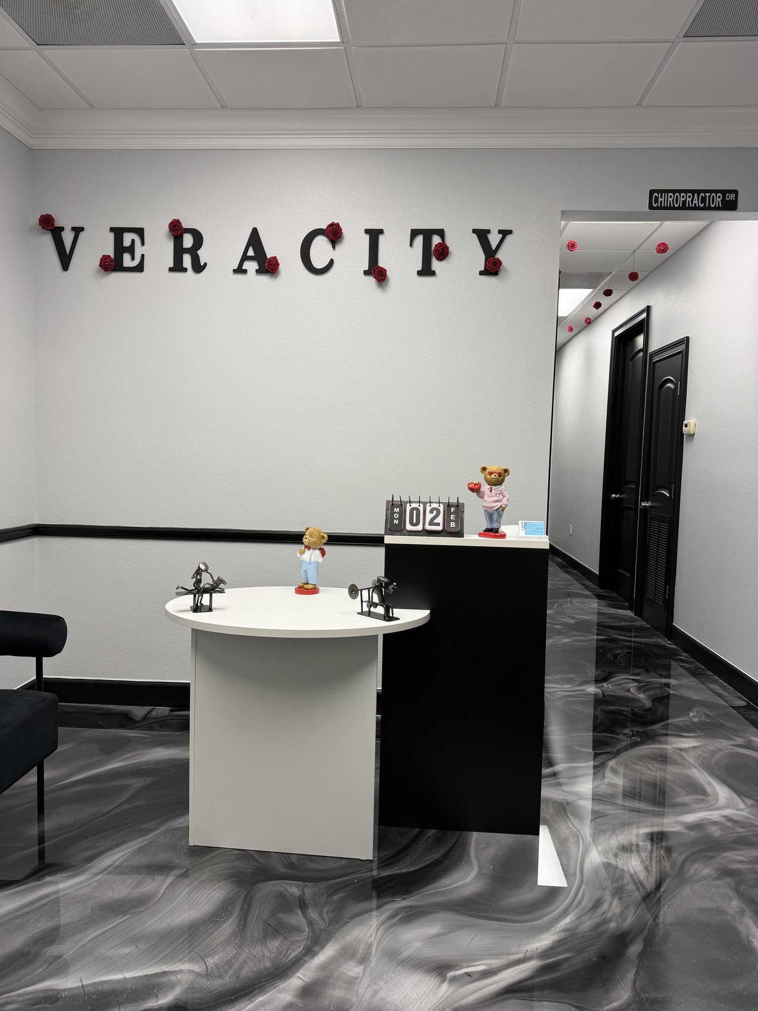 Black and white marbled metallic floor with a high gloss in a chiropractic office reception area, a round white table and a black counter against gray walls