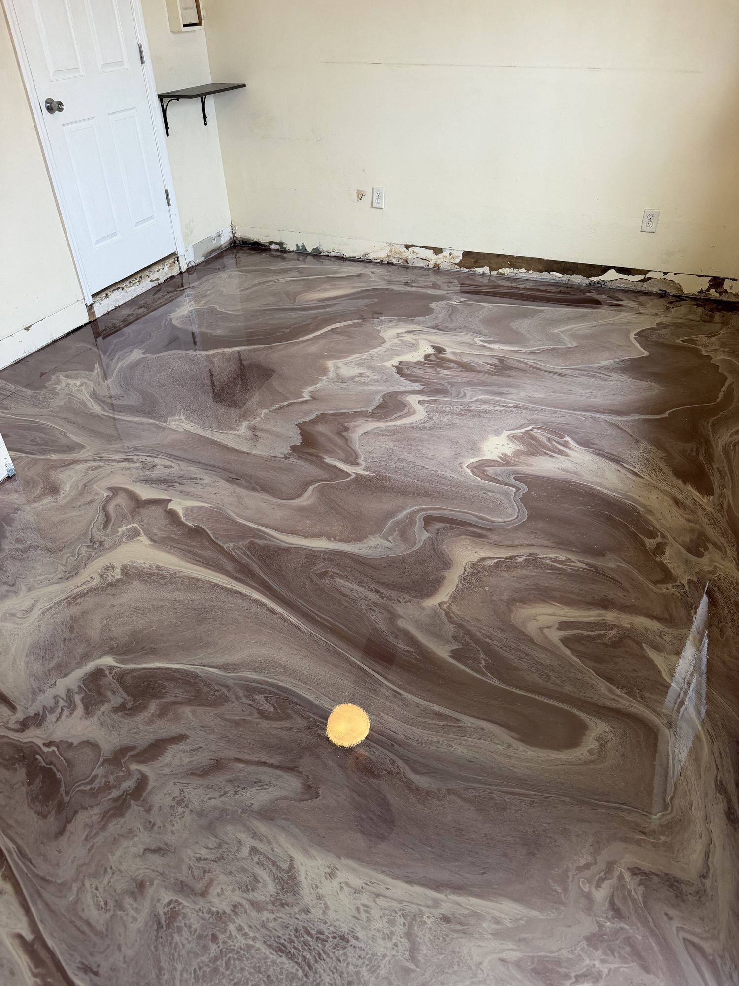 Warm copper and bronze metallic epoxy poured across an interior room, baseboards still off the wall