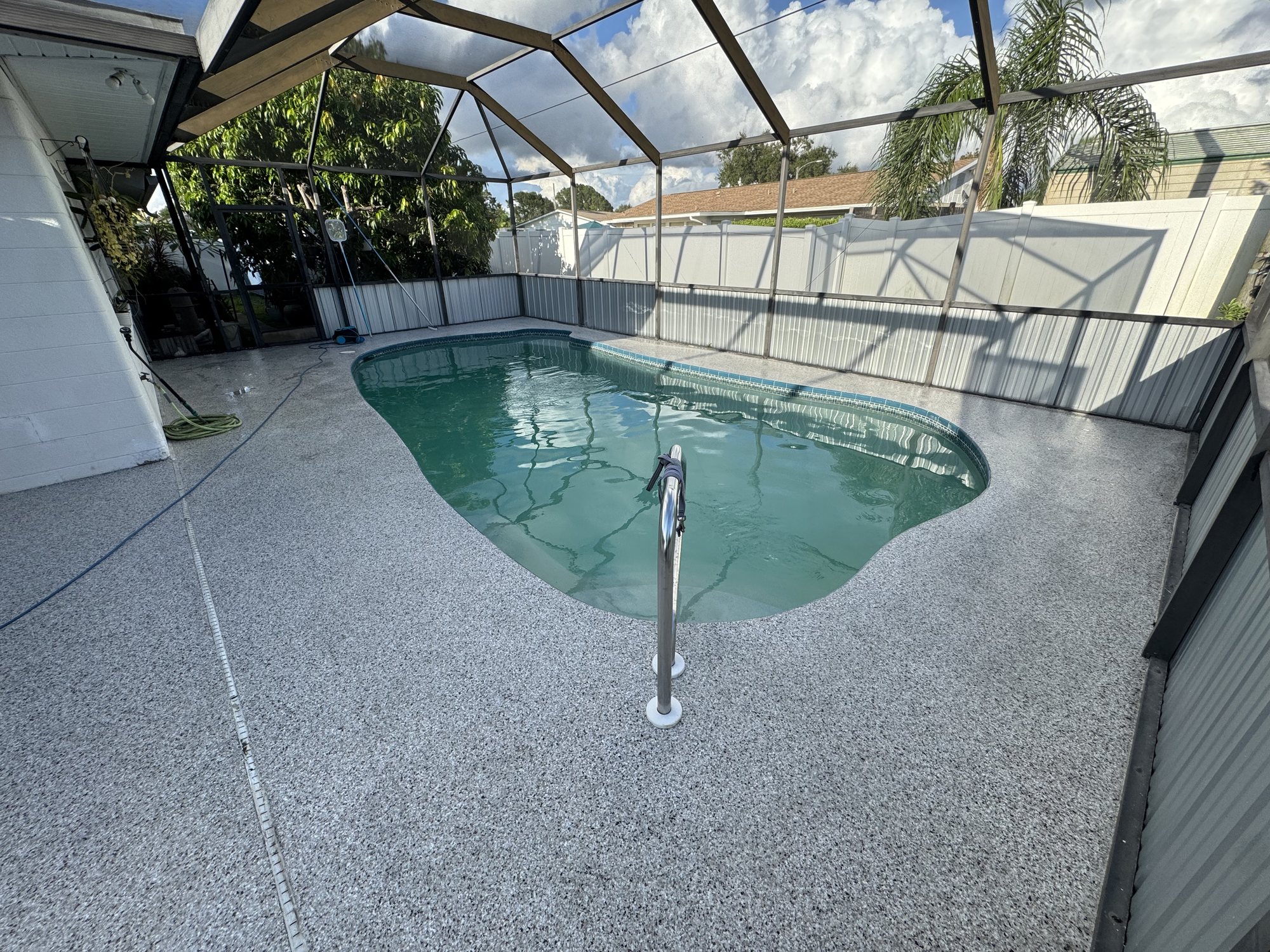 Gray flake coating on a screened lanai pool deck, pool water and a palm-lined yard through the screen