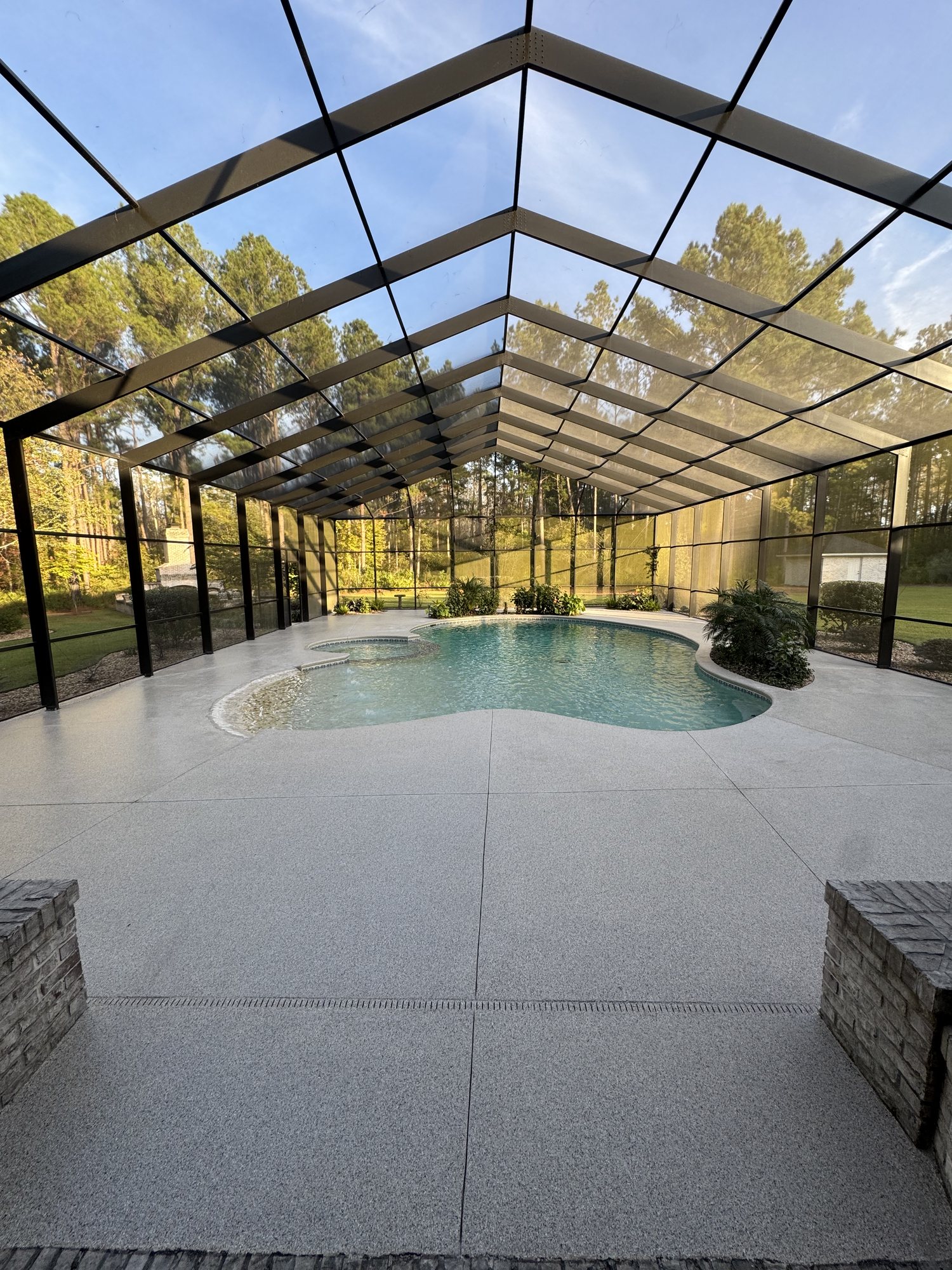 Flake pool deck running to the water's edge inside a screened enclosure, stone planter columns in the foreground